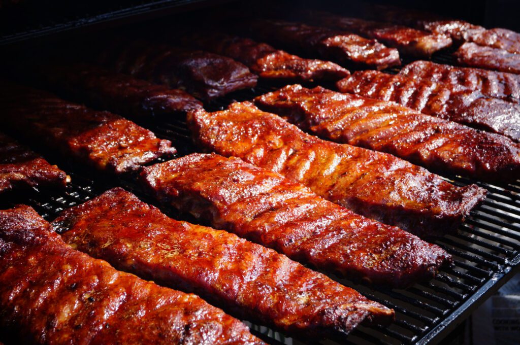 Racks of BBQ ribs slowing cooking on an open grill.